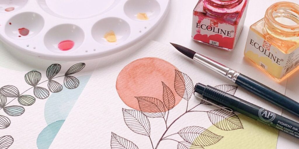 Paint brush, pen and paint palette with artwork showing watercolour and leaf line drawing as an example of an activity for the mindfulness and craft workshop